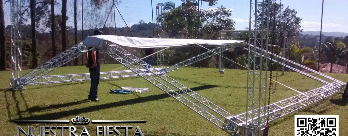 Estrutura semi montada da tenda NUESTRA FIESTA em um campo de futebol, demonstrando o processo de montagem.